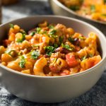 White bowl of macaroni with chili and tomatoes on it