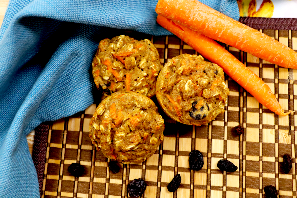 Three carrot muffins on a checkered background next to two whole carrots