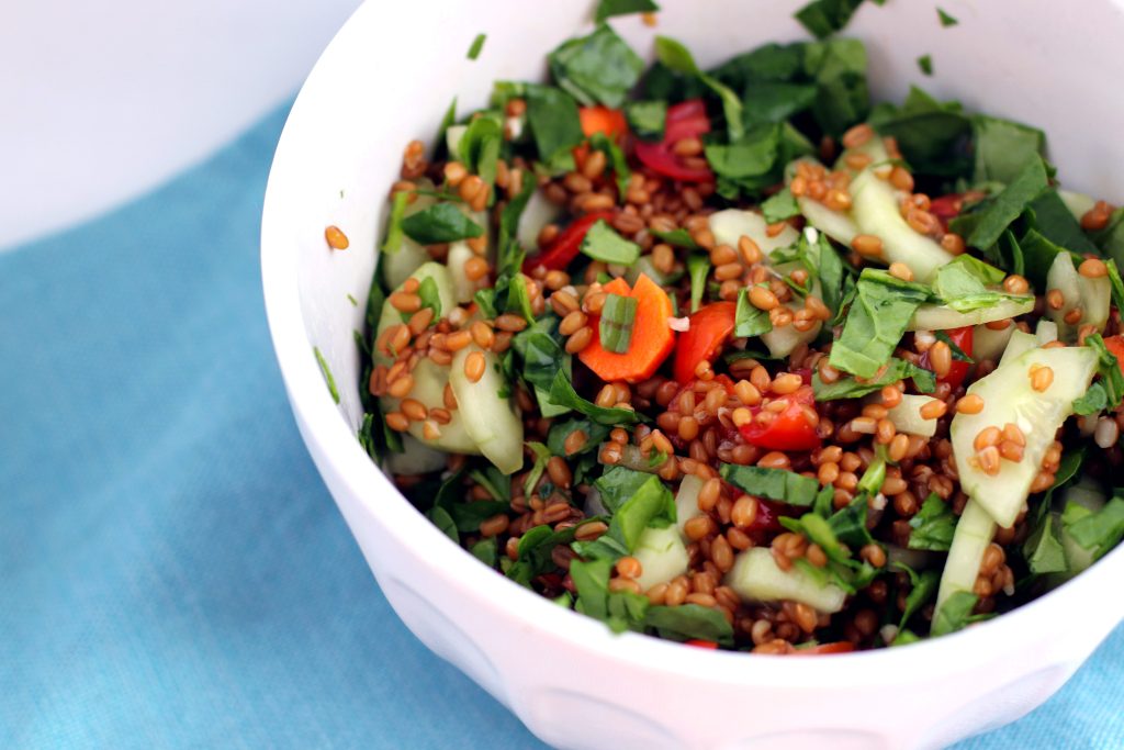 White bowl of cooked grains, leafy greens, and chopped vegetables