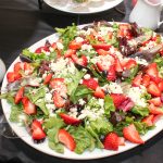 Platter of salad made of spinach and strawberries, topped with nuts and crumbled white cheese