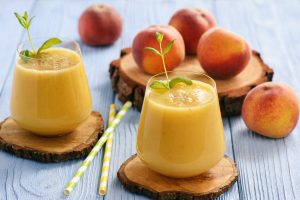 two glasses of peach smoothies with whole peaches in the background
