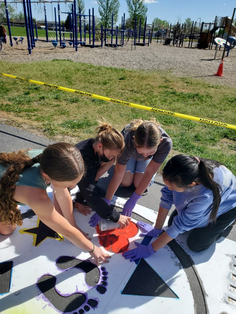 A group of middle school students paint a game on the sidewalk