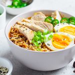 Asian noodle soup with chicken and egg in a gray bowl, topped with green onions