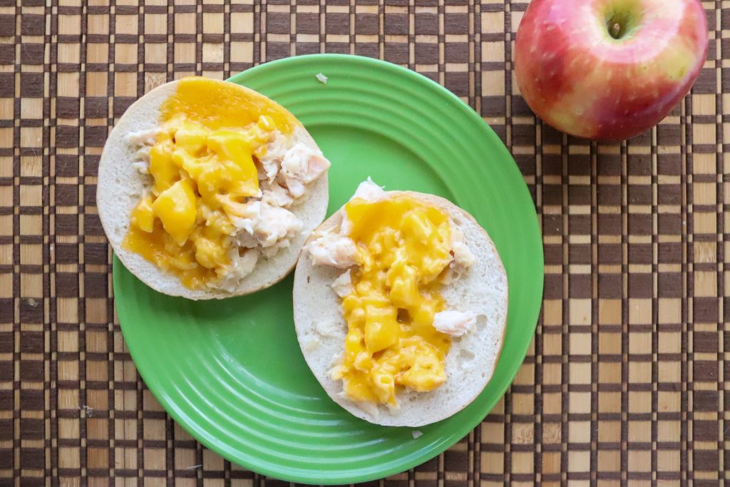 Bagel topped with canned chicken and melted cheese next to an apple