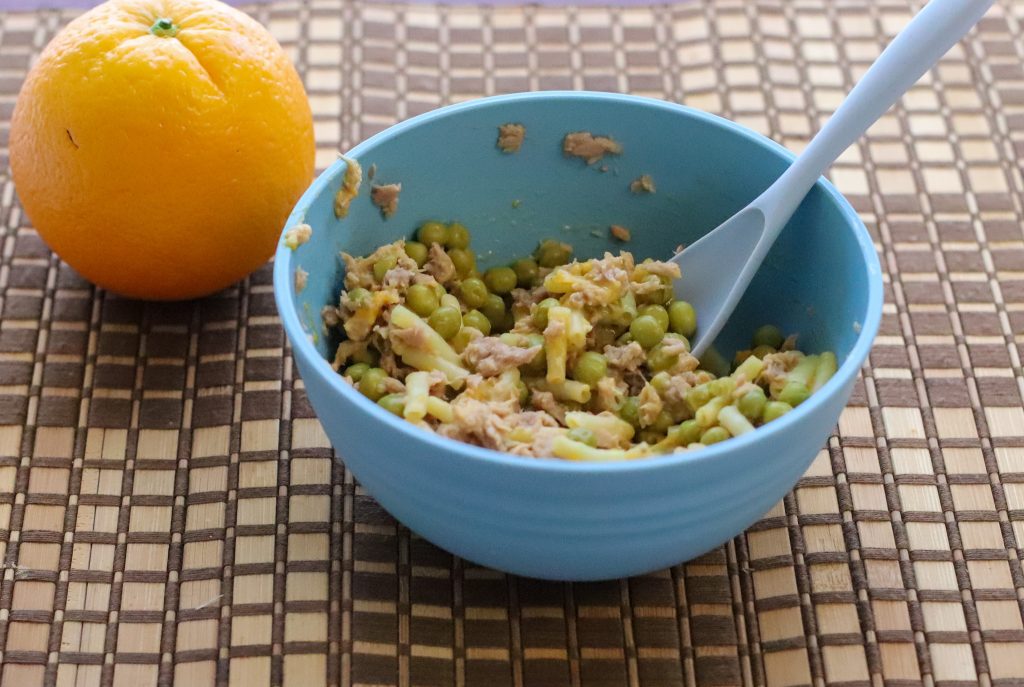 Bowl of microwave mac and cheese with tuna and peas next to an orange