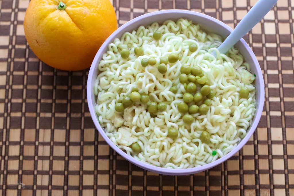Bowl of ramen with canned peas and chicken next to an orange