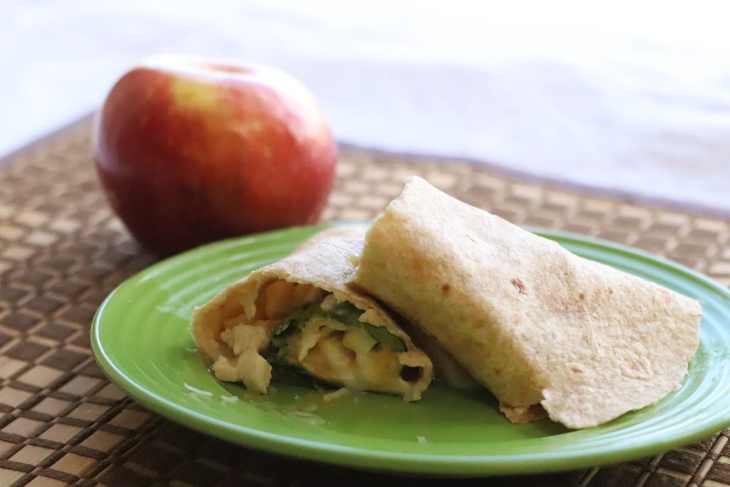 Tortilla wrap with chicken cheese and spinach next to an apple