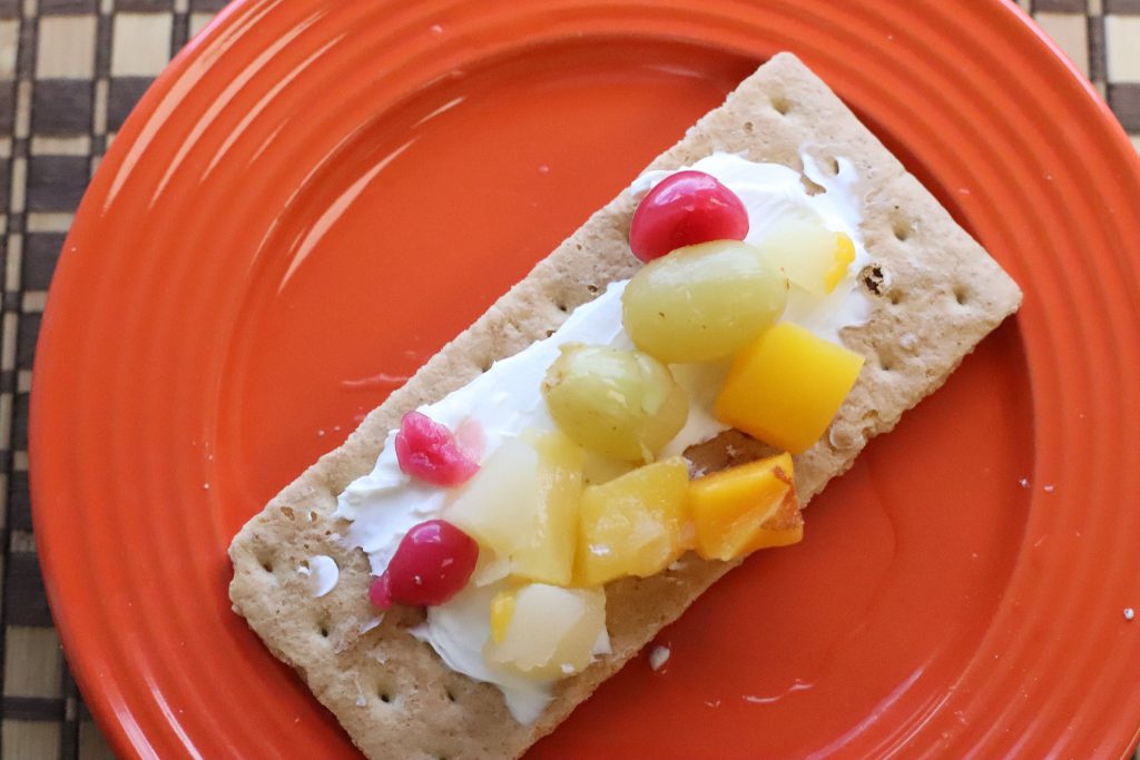 Graham cracker topped with cream cheese and canned fruit