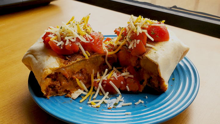 beef and bean burritos topped with tomatoes and cheese on blue plate sitting on office desk.