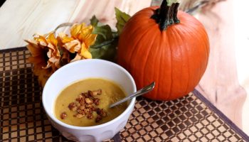 Bowl of pumpkin soup next to a pumpkin and flowers.